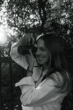 Black-and-white portrait of Emma Tysinger holding a camera beneath trees.