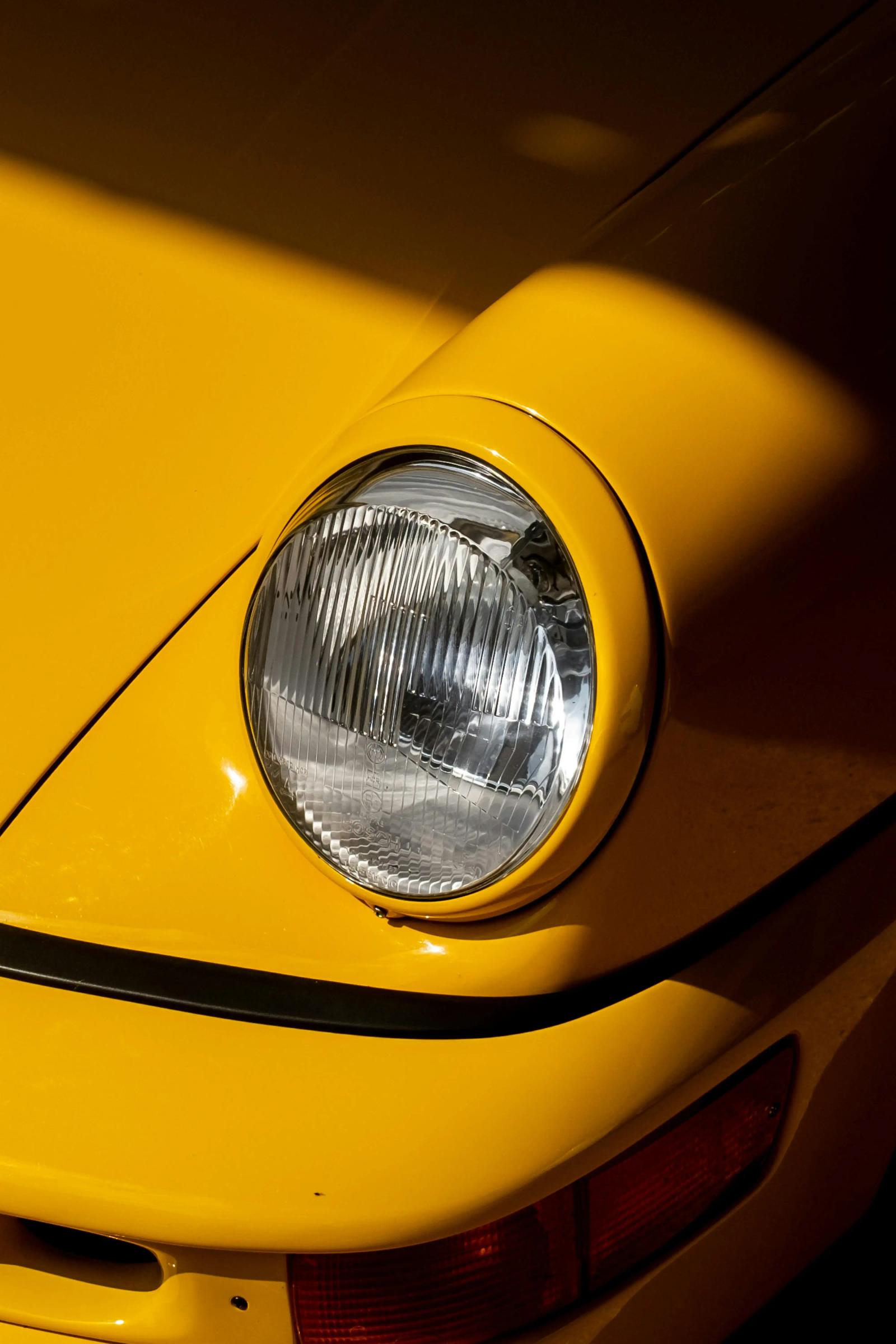 A yellow Porsche 911 headlamp in sharp shadow.