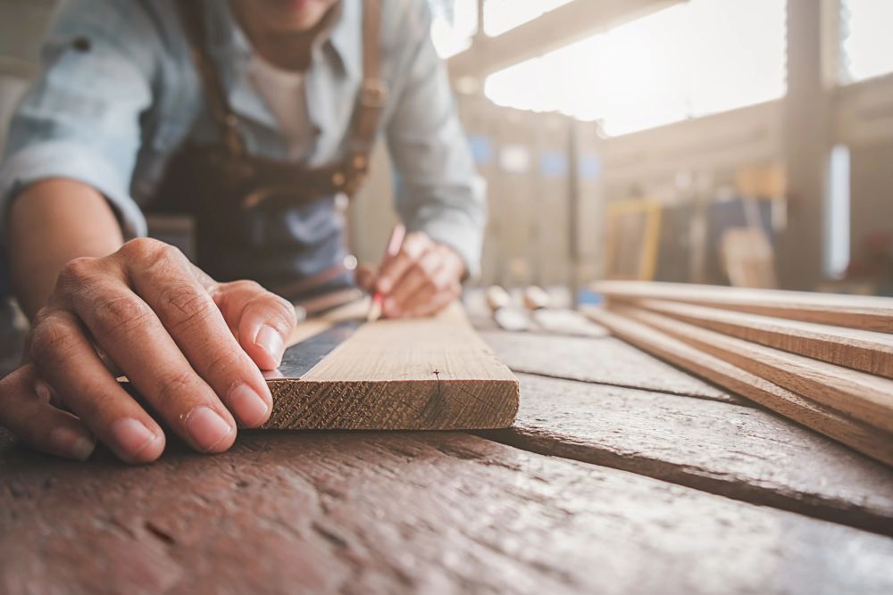 Close-up of a carpenter measuring and marking wood to craft custom picture frames in a workshop.