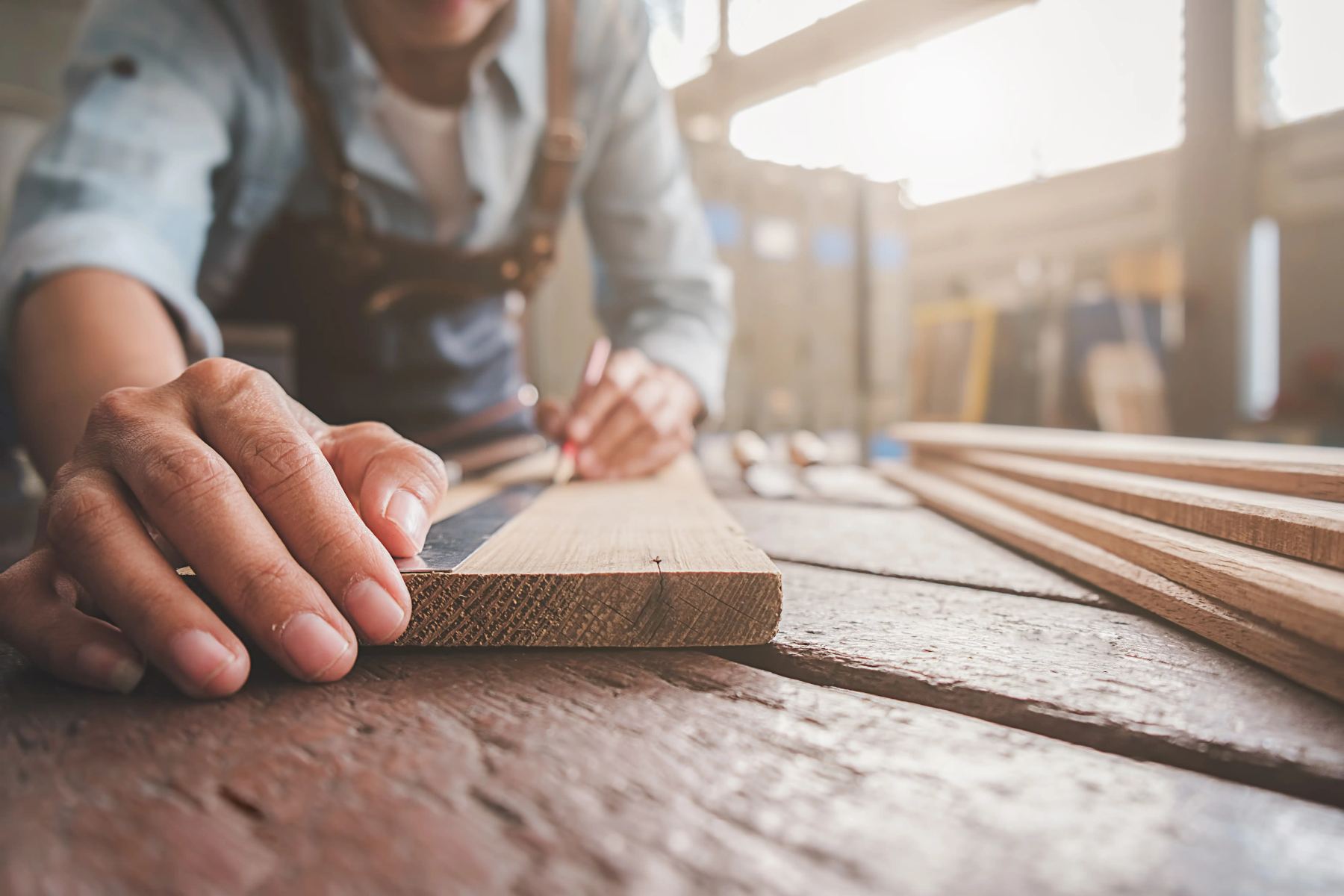 Close-up of a carpenter measuring and marking wood to craft custom picture frames in a workshop.