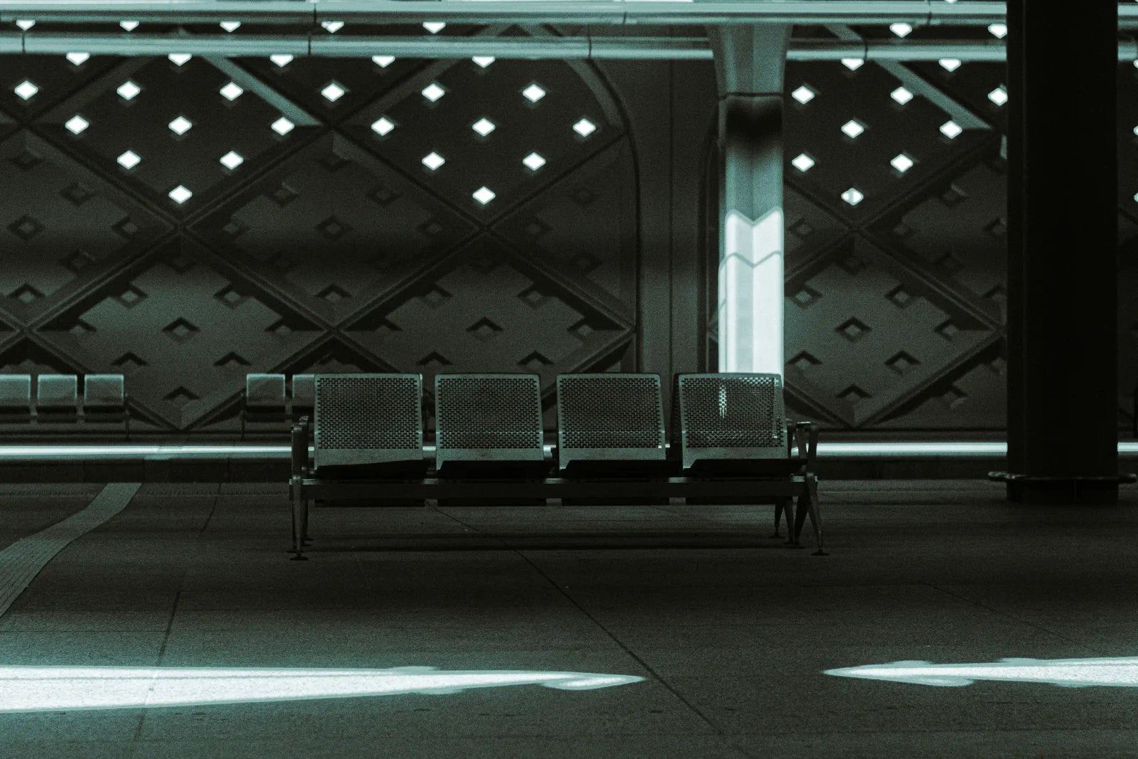 Empty metal seats beneath a geometric station canopy, with a shaft of sunlight crossing the floor.
