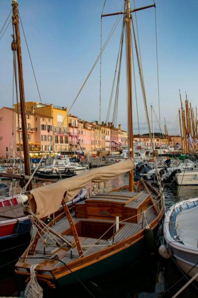 Classic wooden sailing boat moored in St Tropez harbour with colourful Mediterranean buildings
