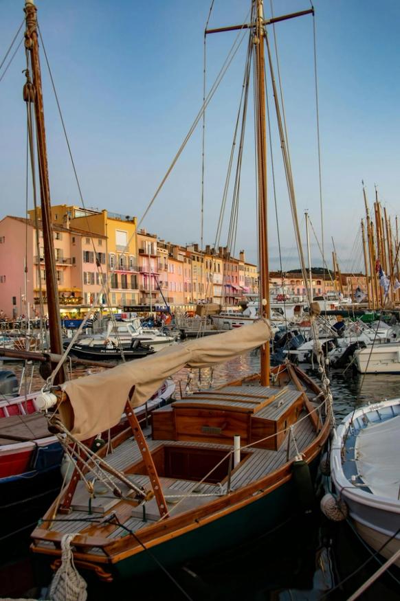 Classic wooden sailing boat moored in St Tropez harbour with colourful Mediterranean buildings
