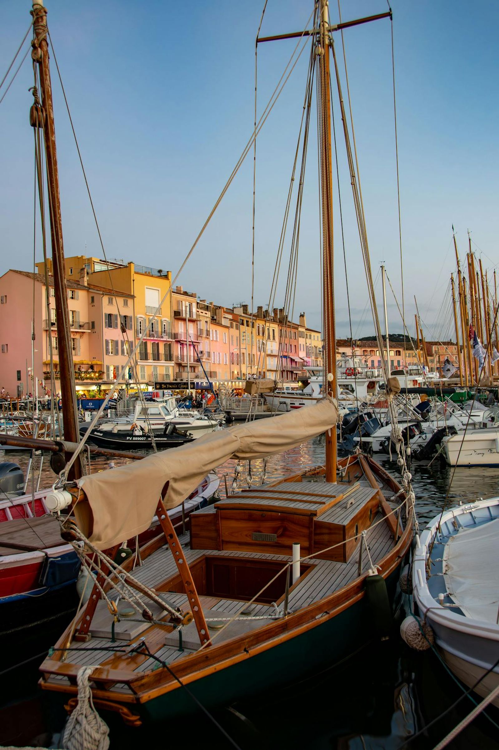 Classic wooden sailing boat moored in St Tropez harbour with colourful Mediterranean buildings
