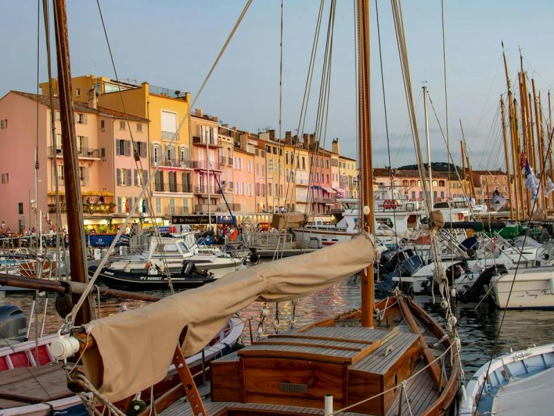 Classic wooden sailing boat moored in St Tropez harbour with colourful Mediterranean buildings