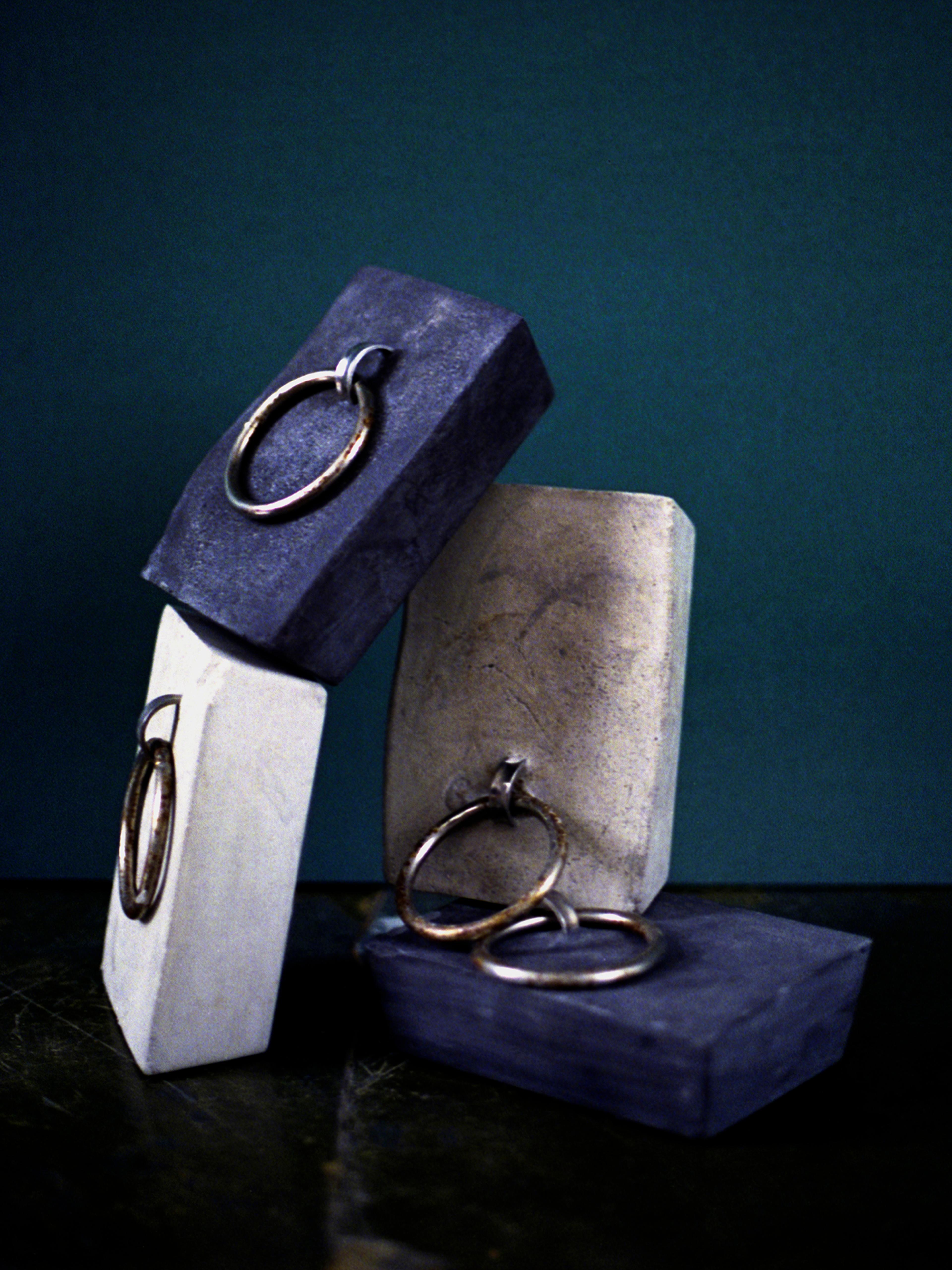 three concrete blocks set with metal rings, leaning together against a teal wall