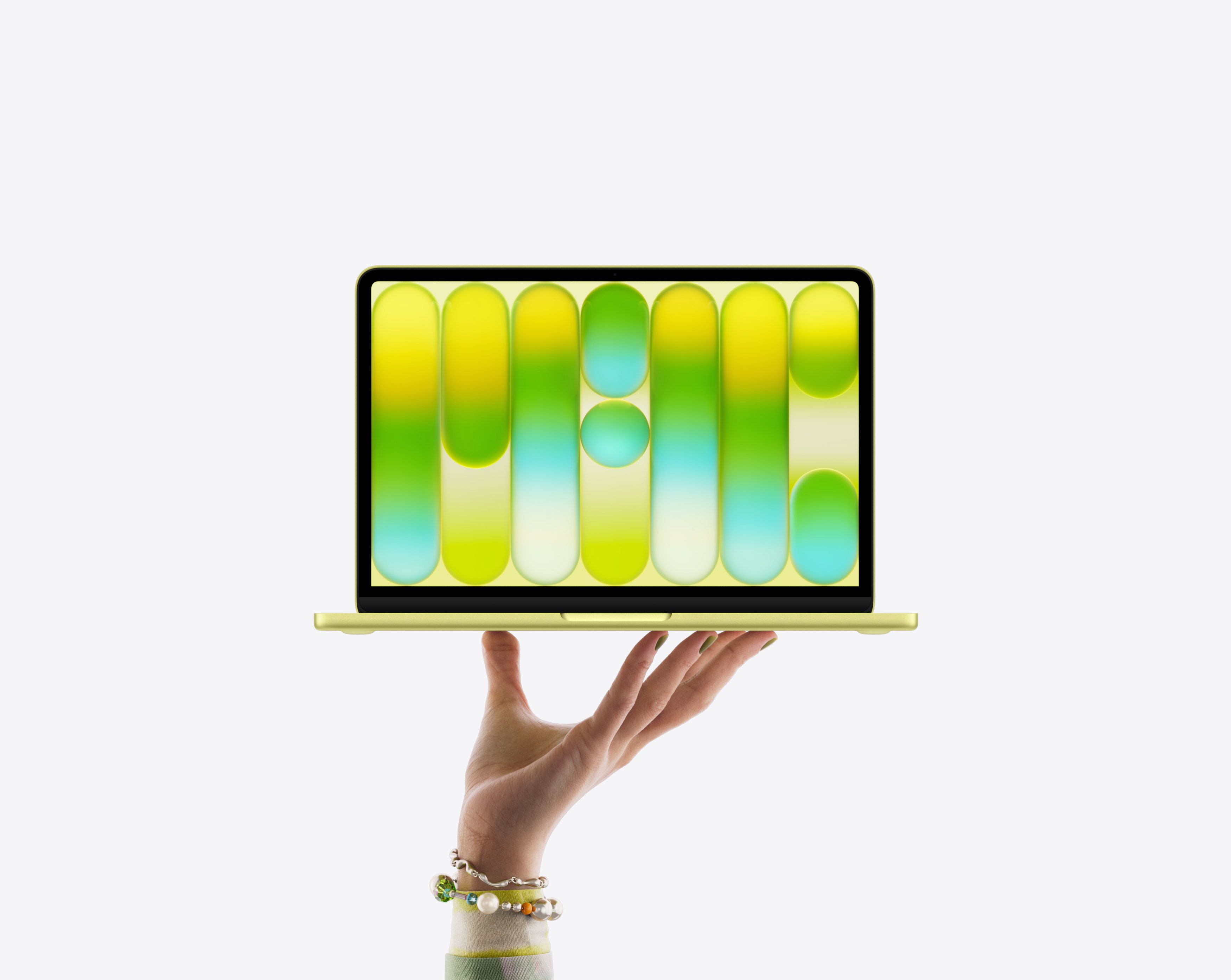 MacBook Neo couleur jaune agrume, en équilibre sur le bout des doigts d’une main ouverte, écran affichant un motif abstrait coloré