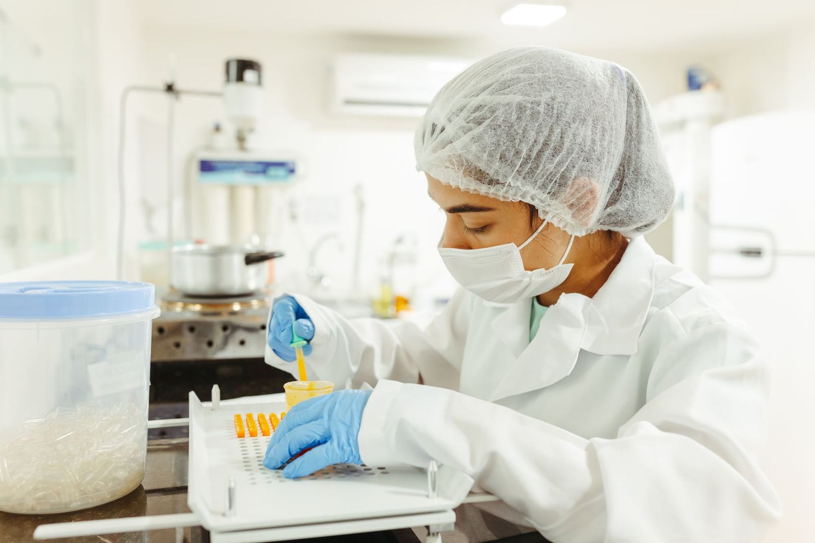 Científica preparando muestras en un laboratorio con gorro y barbijo