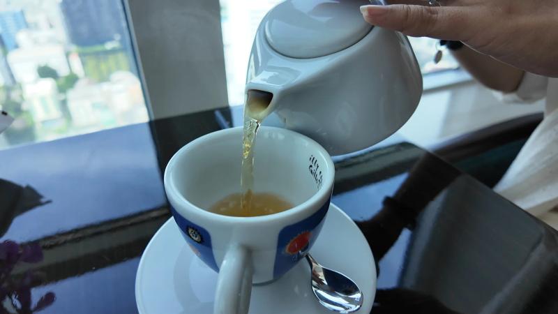 Tea being poured from a white pot into a blue and white cup at a window table high above Sukhumvit.