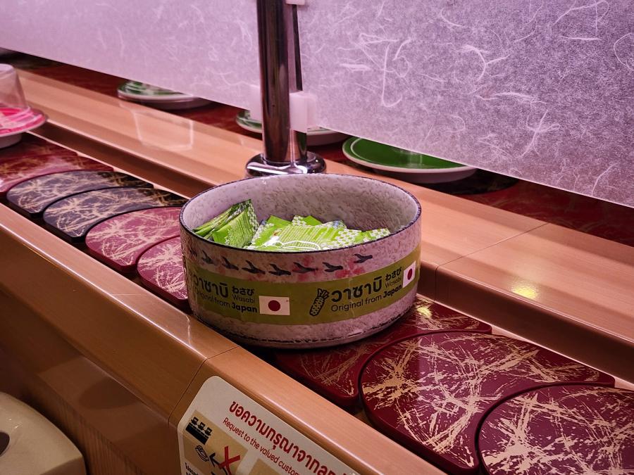 A speckled ceramic bowl of green wasabi sachets on the counter beside the belt, labelled wasabi original from Japan.