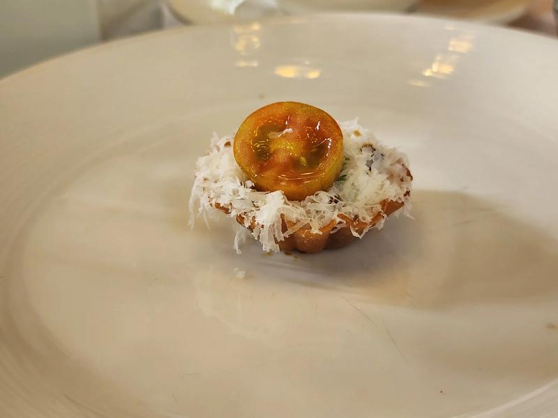 A small fluted tart covered in grated white cheese with half a glazed cherry tomato on top.