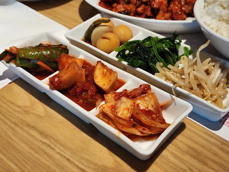 Two trays of Korean side dishes: cucumber kimchi, radish kimchi, cabbage kimchi, quail eggs, spinach and bean sprouts.