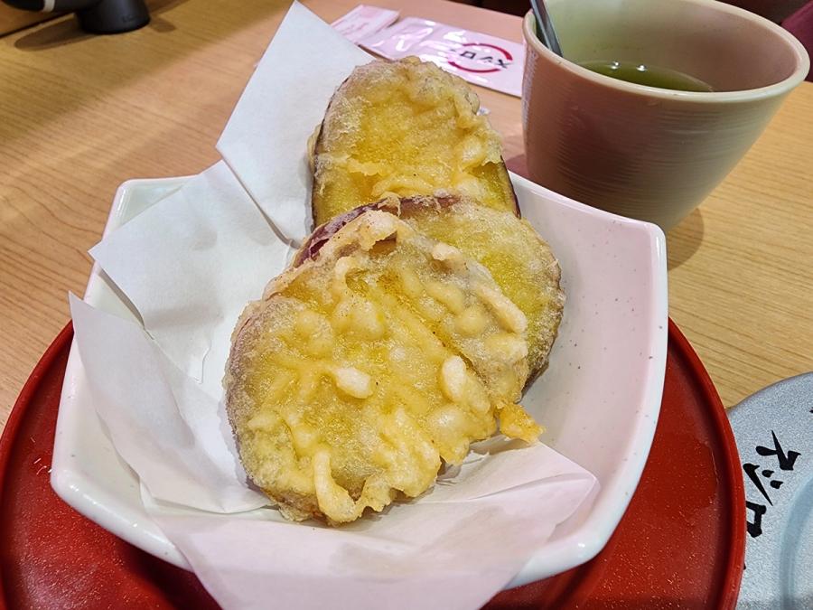 Three pieces of sweet potato tempura in a paper-lined dish beside a cup of green tea.