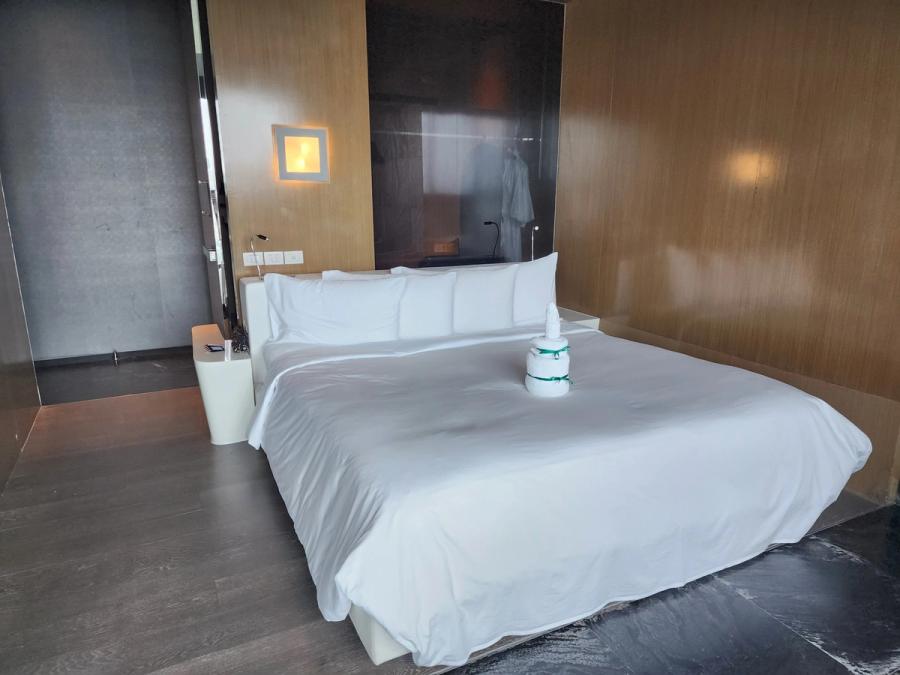 King bed at SO/ Bangkok with white bedding and a folded towel cake tied with green ribbon.