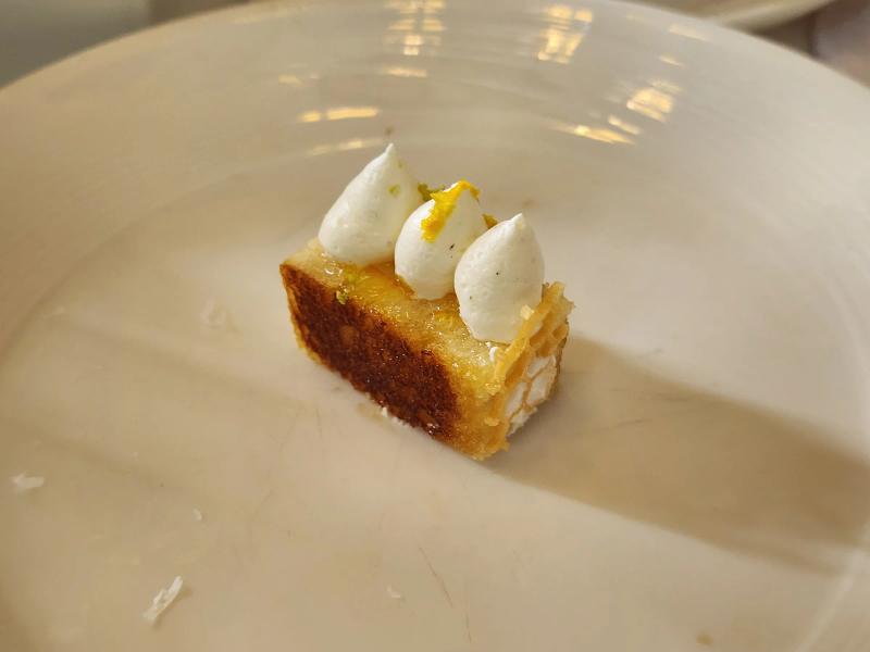 A small toasted square of bread topped with three piped dots of white cream and a strip of orange zest.