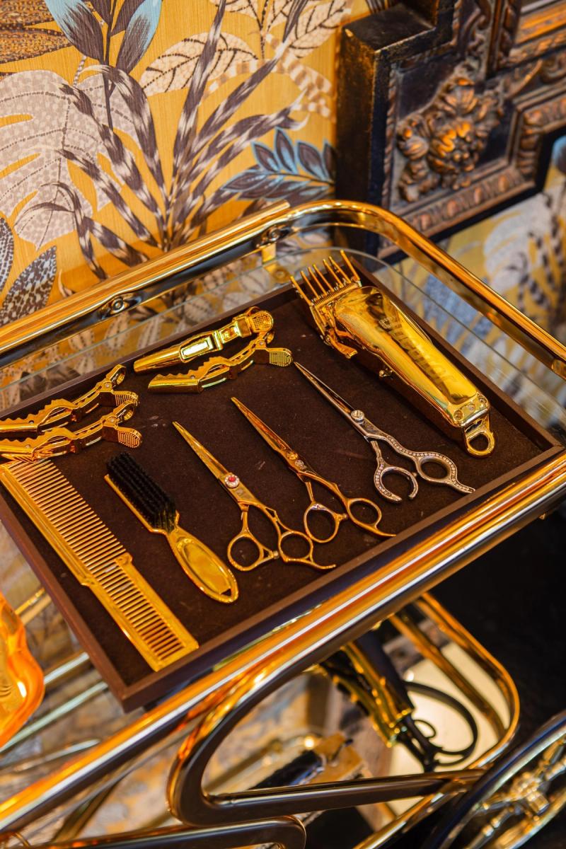 Gold-plated scissors, combs and clippers laid out on a felt-lined tray on a gold trolley at Libertish Salon Cafe.