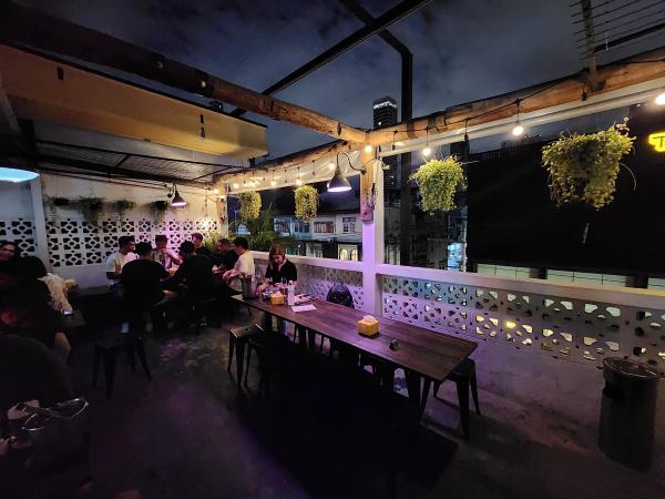 The rooftop terrace at Friendly Stranger at night, with a long timber table, white breeze block walls, hanging plants and a group drinking at the far end.