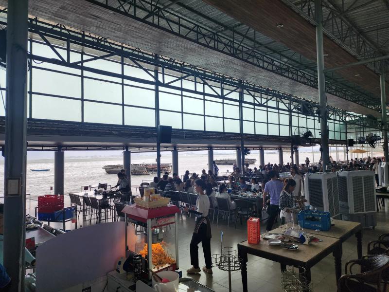 The open dining hall at Moom Aroi with a popcorn machine in the foreground, staff at work and diners at tables along the sea.