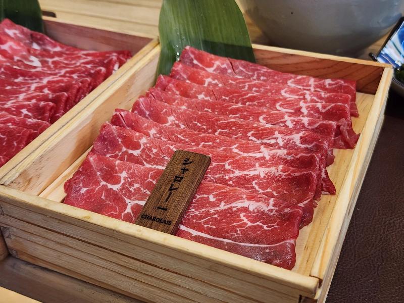 A wooden box of thinly sliced Charolais beef on a bamboo leaf with a dark wooden tag reading Charolais.