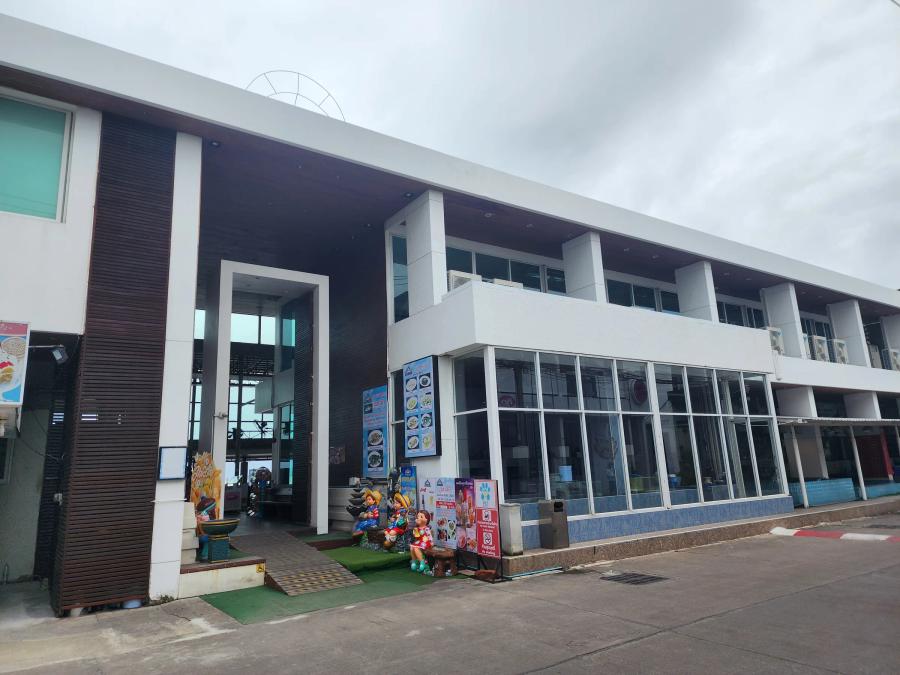 The white two-storey entrance building at Moom Aroi with a dark timber porch, cartoon statues and menu boards beside the door.