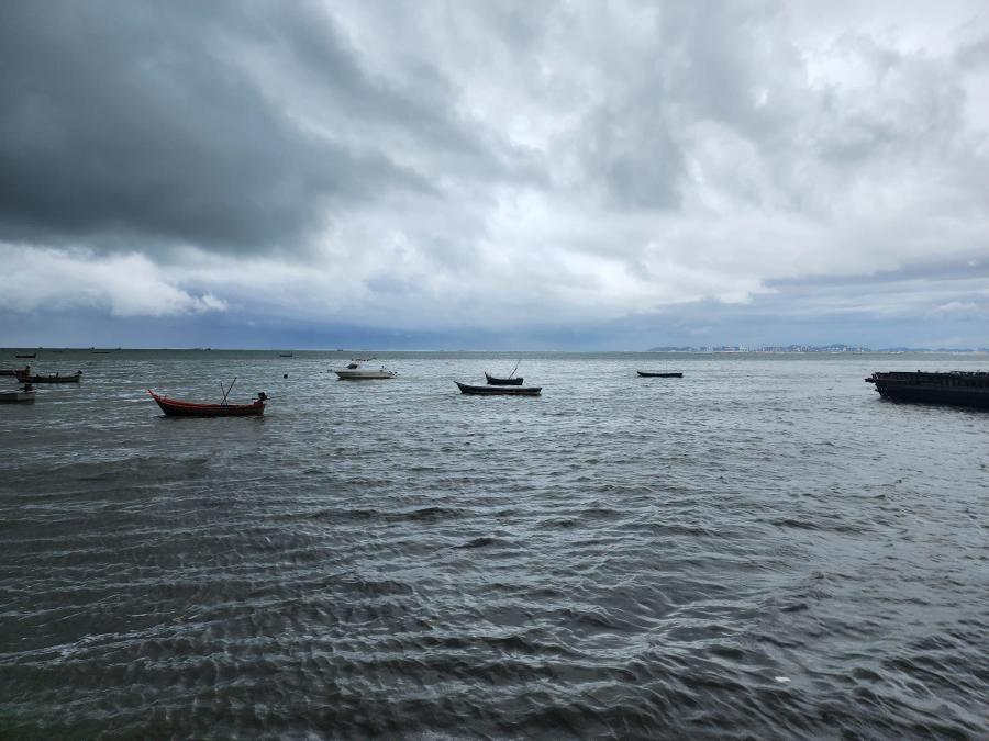 Small fishing boats at anchor on a grey sea under heavy cloud, with a distant shoreline on the horizon.