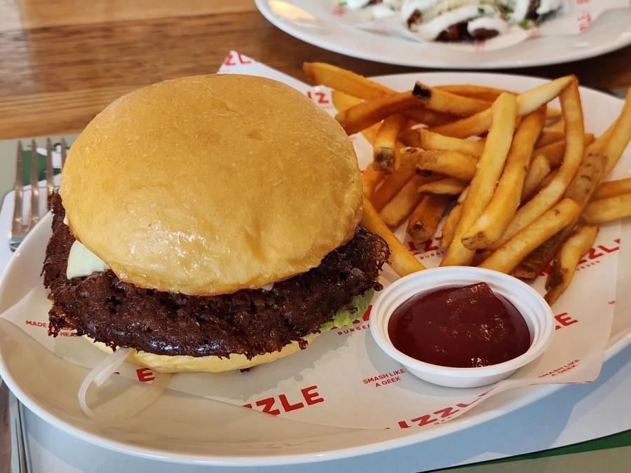 A Smizzle smash burger with a charred beef patty beside french fries and a pot of ketchup.