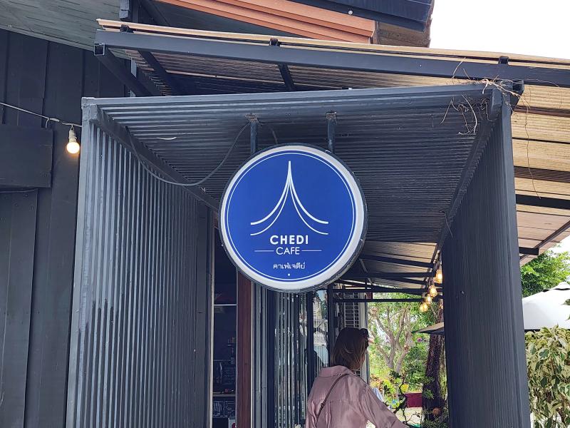 A round blue Chedi Cafe sign with a white spire outline hanging under a corrugated roof over the entrance walkway.
