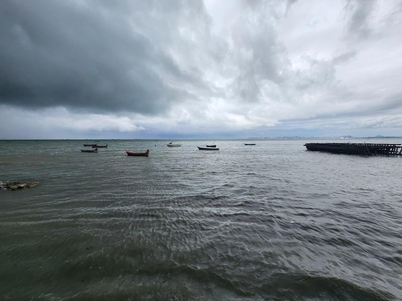 A wide view of fishing boats at anchor on a grey sea off Naklua under heavy cloud, with a timber raft at the right.