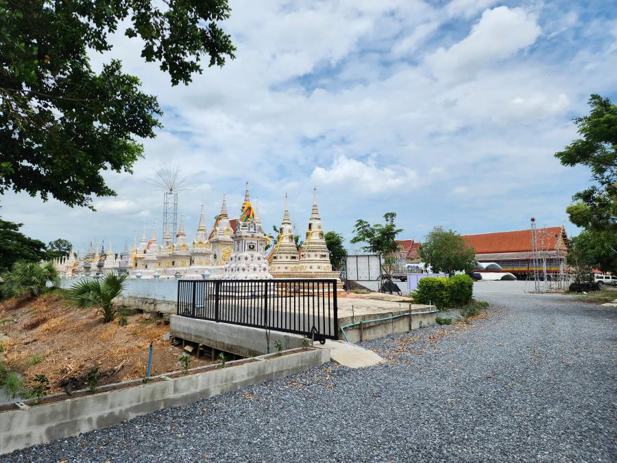 A row of white and gold chedis of different heights at Wat Thong Pradit under a cloudy sky, with a temple hall roof behind.