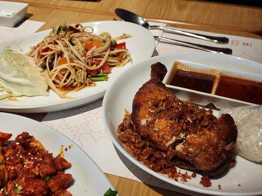 Half a fried chicken covered in crispy fried garlic with two dipping sauces, beside a plate of papaya salad with cabbage.