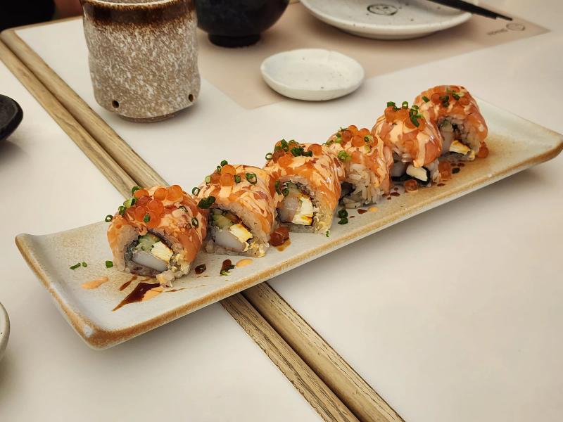 Six pieces of a salmon-topped sushi roll with salmon roe and spring onion on a long speckled plate at Shichi Japanese Restaurant.