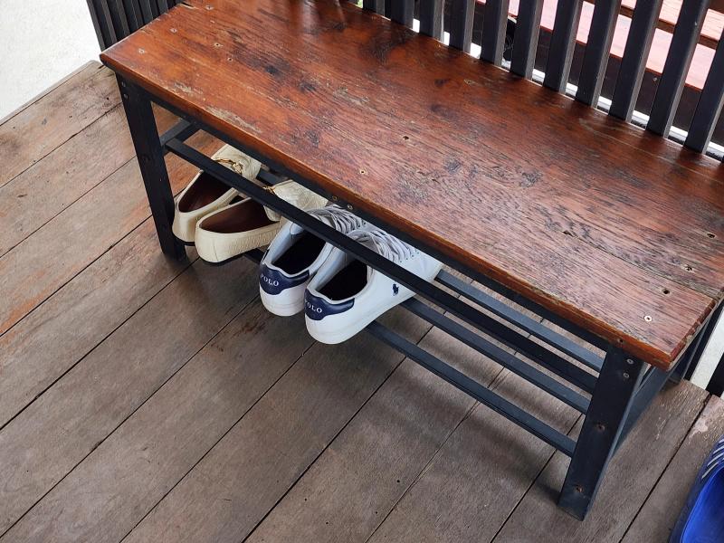 A wooden shoe bench on a deck at Cafe Chedi with two pairs of shoes stored on the rack underneath.