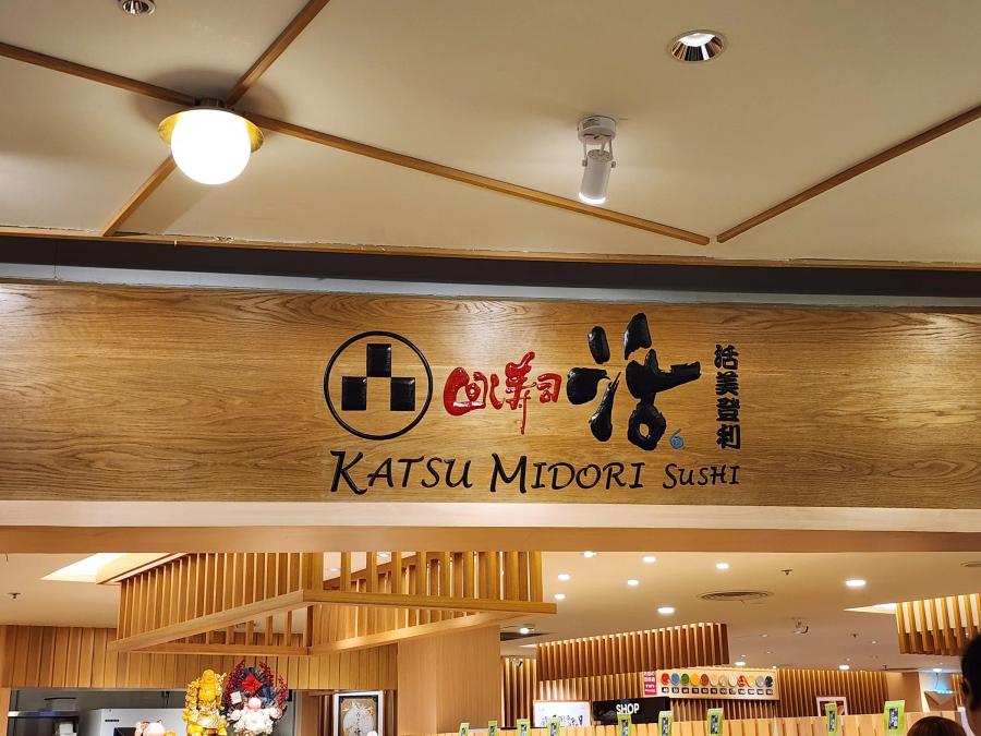 The wooden Katsu Midori Sushi name board above the entrance, with slatted wood panels and the takeaway shop sign underneath.