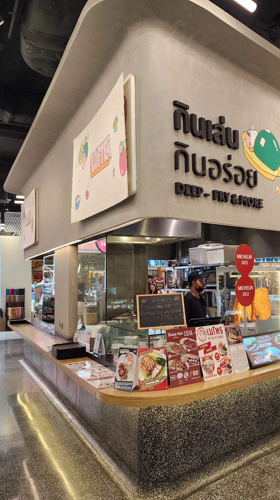 A curved concrete food counter at LOFTER with Thai lettering above it and red Michelin plaques beside the till.