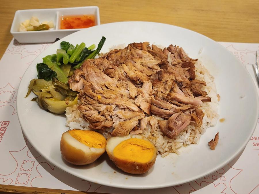 Shredded stewed pork knuckle over rice with pickled greens, Chinese kale and a halved braised egg.