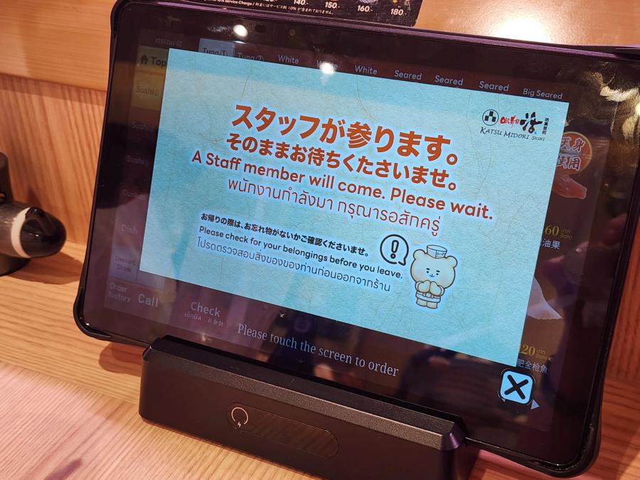 The ordering tablet showing a message in Japanese, English and Thai that a member of staff will come, with menu tabs for tuna, white fish and seared sushi along the top.