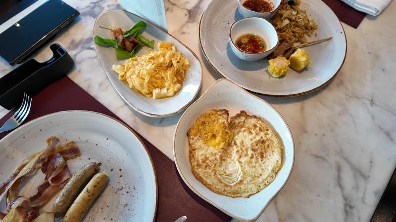 Plates of bacon and sausages, fried eggs, scrambled eggs and fried rice with dim sum on a white marble table at Bella Sera.
