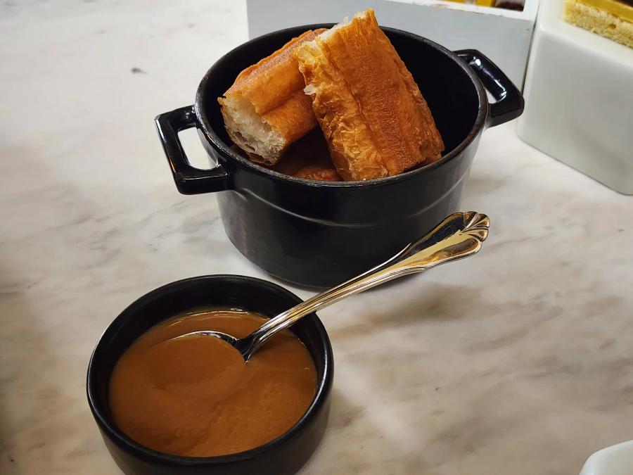 Pieces of golden fried dough in a small black cast iron pot, with a bowl of caramel-coloured dip and a silver spoon in front.