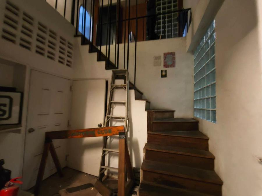A bare stairwell with worn timber steps, a stepladder and a wooden sawhorse on the landing, glass blocks in the wall and posters higher up.