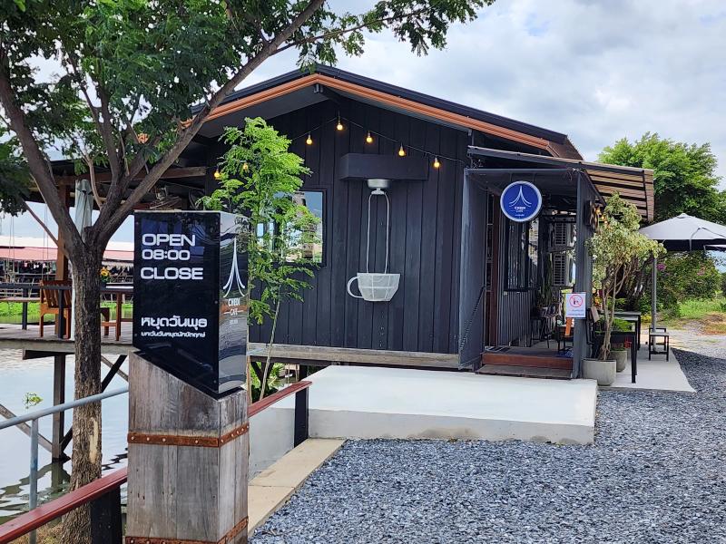 A black sign at the gate of Cafe Chedi reading open 08:00 with the closing time blank, in front of the timber cafe.