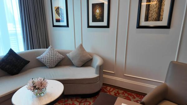 The curved cream sofa in the living room of Junior Suite 2305 at Sofitel Bangkok Sukhumvit, with patterned cushions, flowers on a round marble table and three framed prints above.