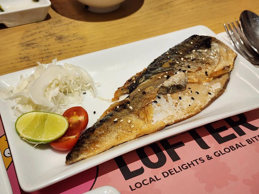 A grilled mackerel fillet sprinkled with sesame seeds on a white plate with shredded cabbage, tomato and lime.