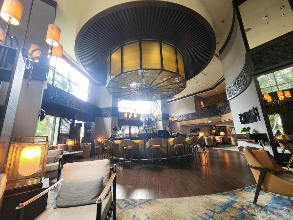 The round Diplomat Bar at Conrad Bangkok under a large amber ceiling lantern, with bar stools, tall windows onto greenery and an armchair in the foreground.