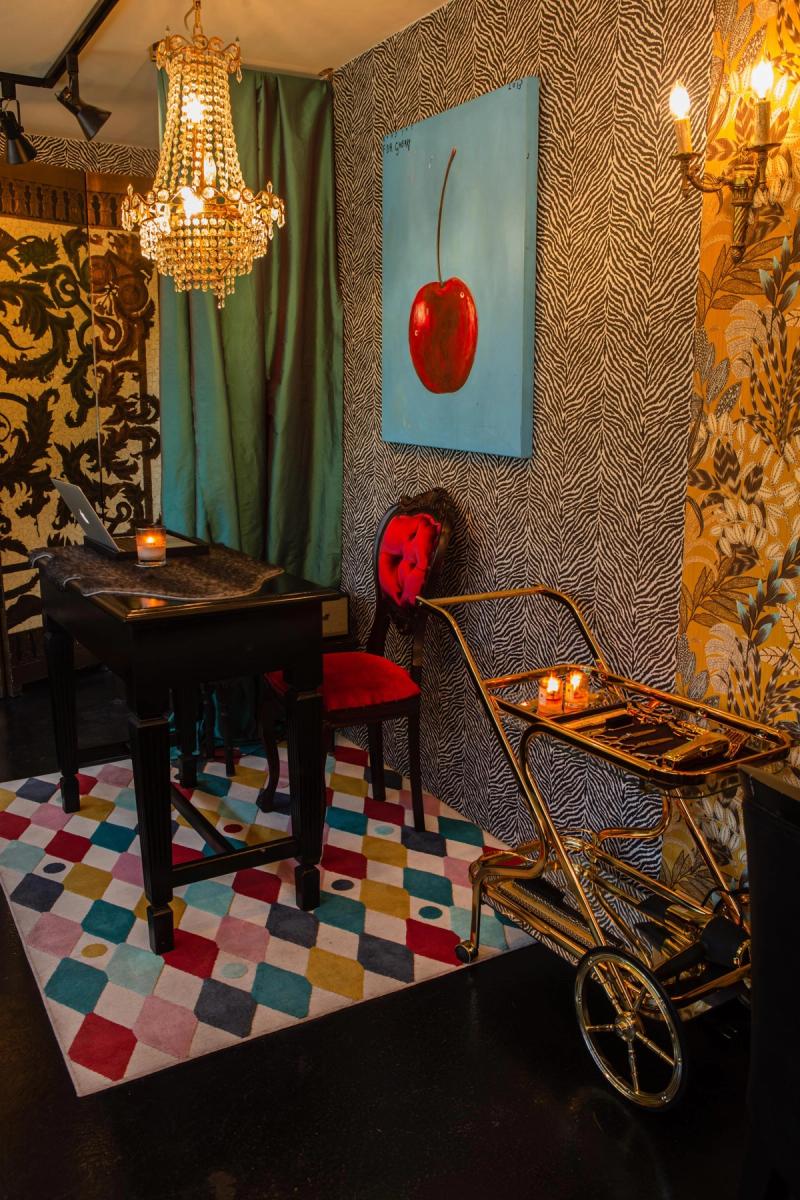 A salon corner with zebra-print wallpaper, a gold trolley, a red velvet chair and a large cherry painting on a teal canvas at Libertish Salon Cafe.
