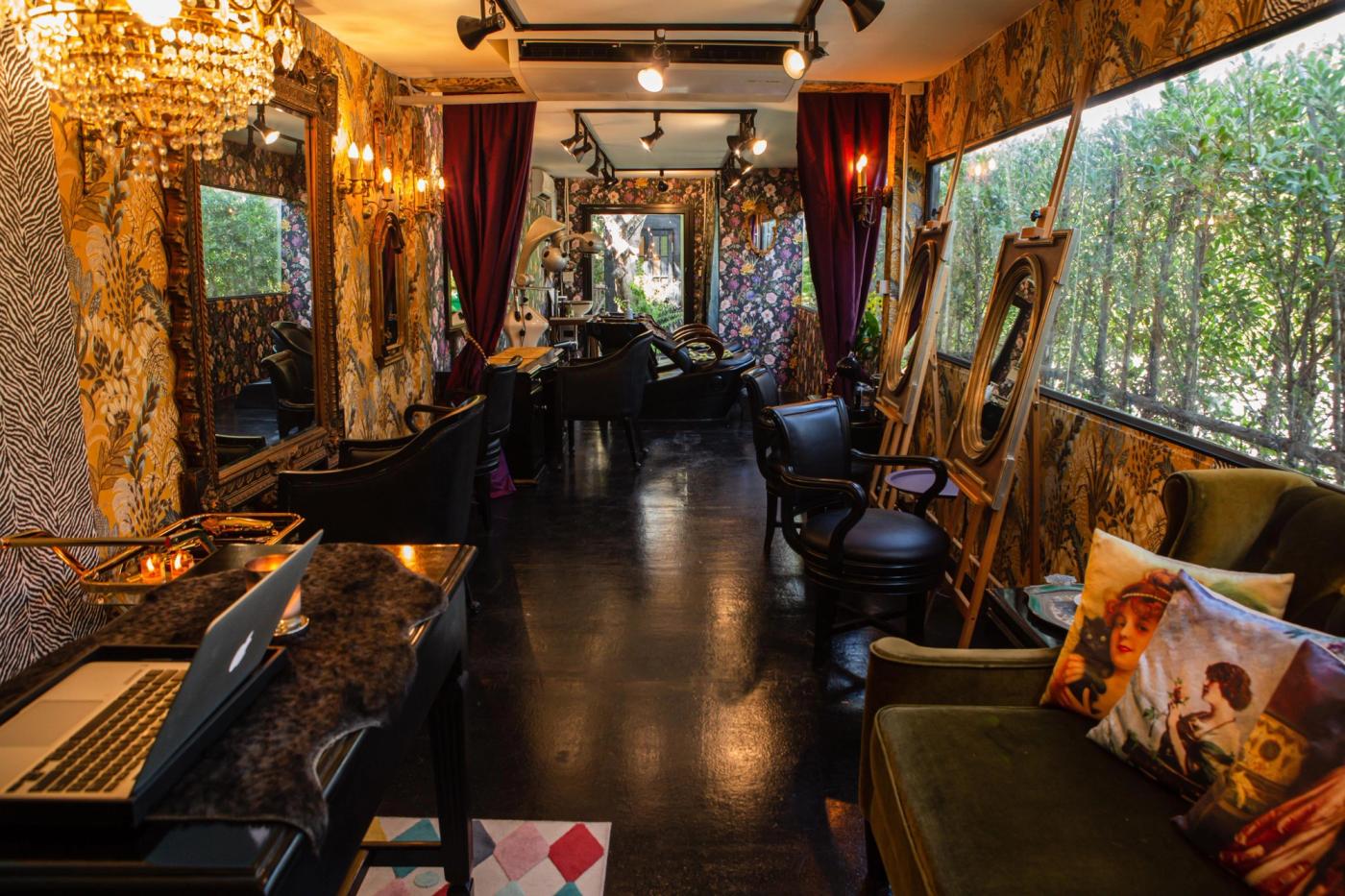 Looking down the length of Libertish Salon Cafe. Crystal chandeliers, dark floral wallpaper and black styling chairs line both sides of the narrow room.
