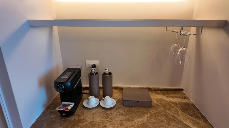 A black capsule coffee machine, two leather-wrapped water bottles, two espresso cups and a leather box on a brown marble minibar counter.