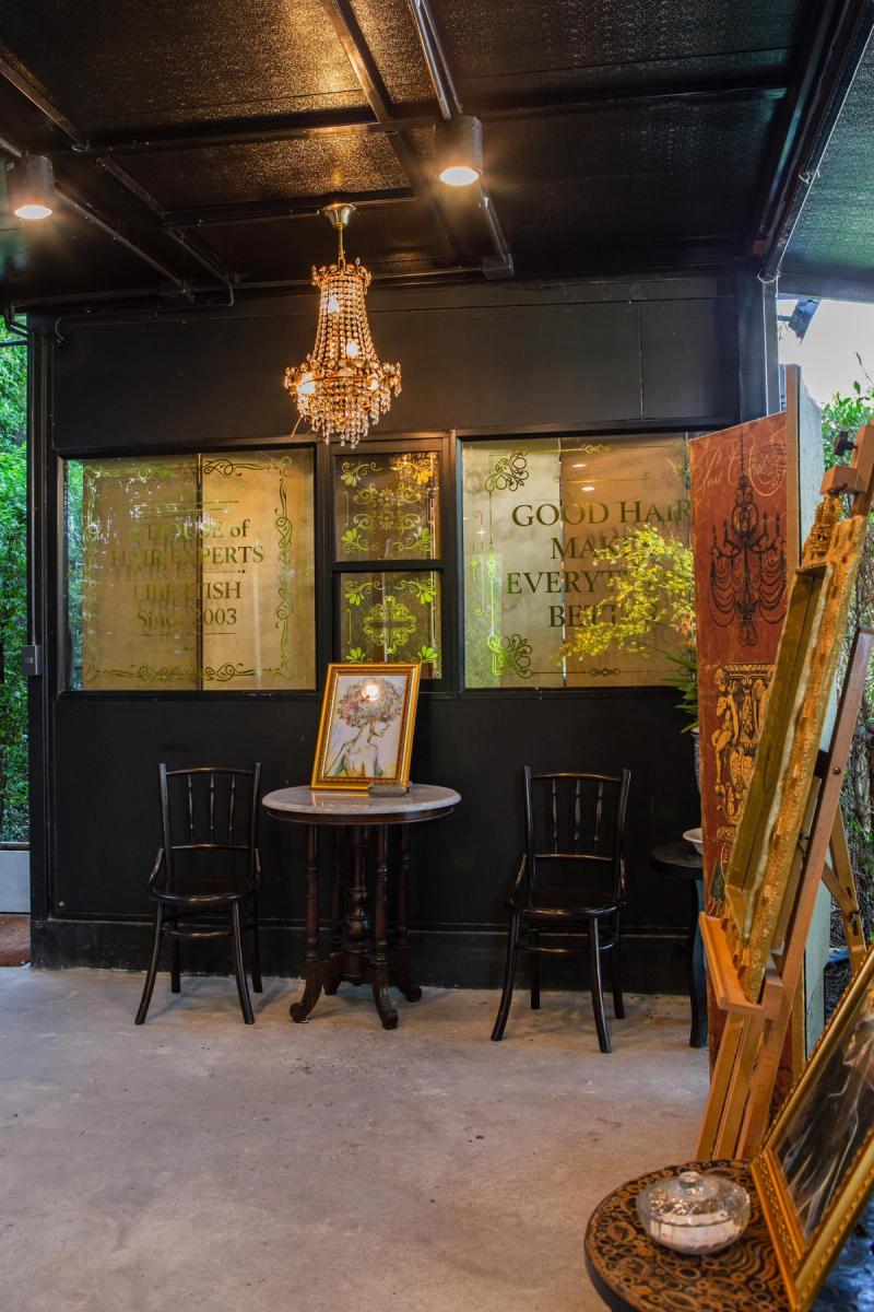 The waiting area at Libertish Salon Cafe, with two black bistro chairs, a marble-top table and a crystal chandelier beneath etched glass panels.