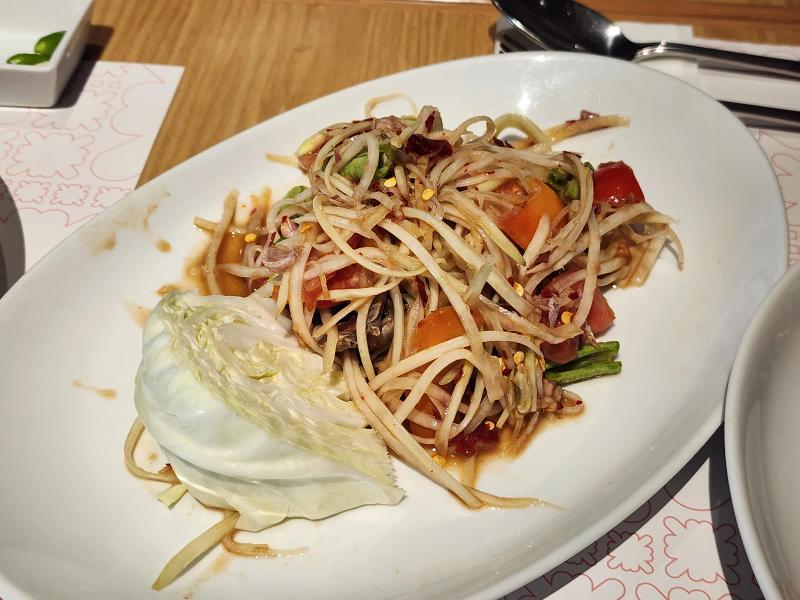 Papaya salad with tomato, long beans and a wedge of raw cabbage on a white plate.
