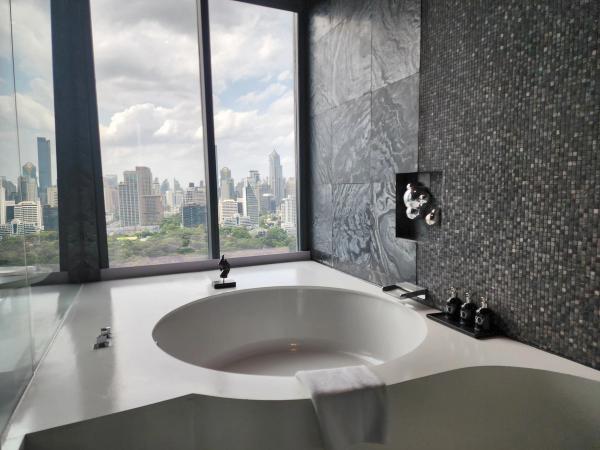 Round bathtub set into a white counter beside floor-to-ceiling windows at SO/ Bangkok, with the city skyline beyond.