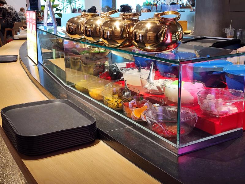 A Thai dessert counter with brass kettles above glass bowls of jellies, fruit and toppings.